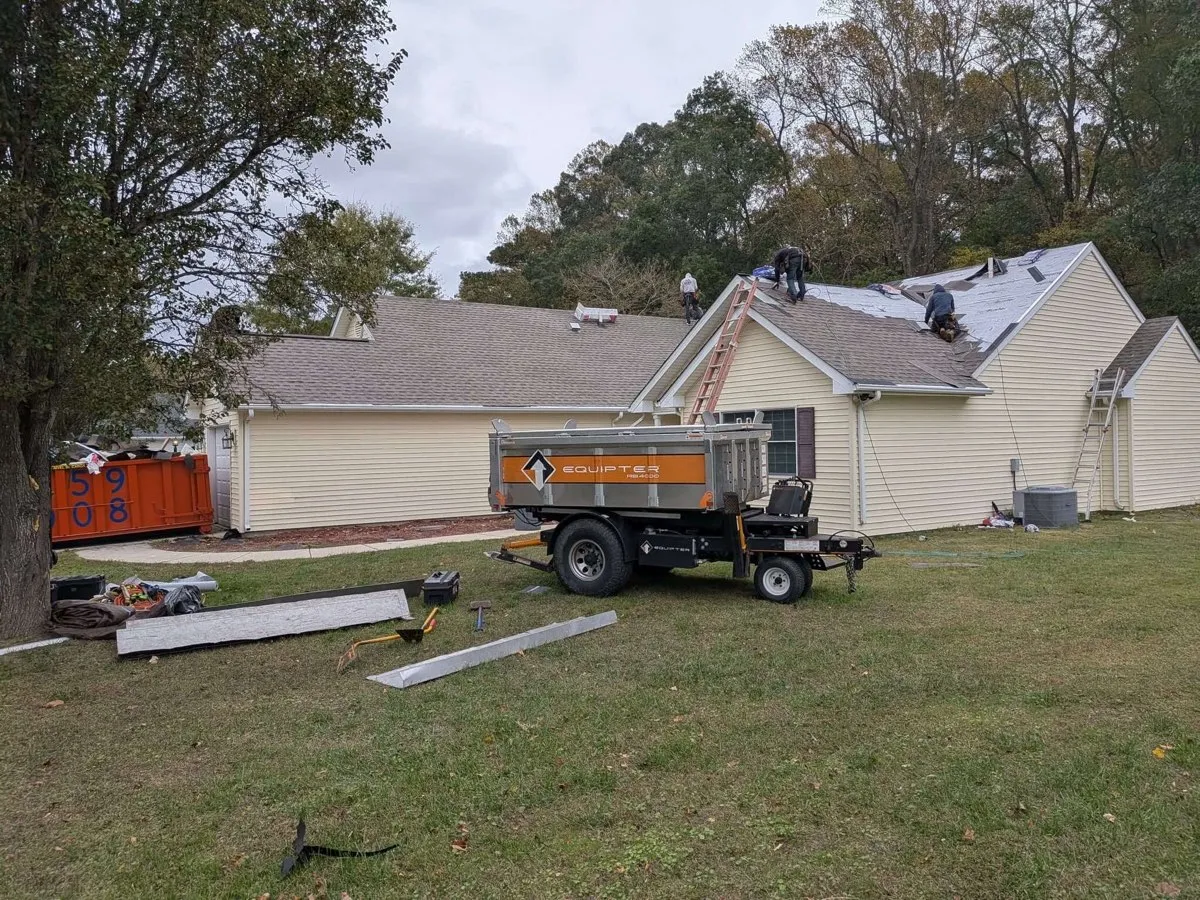Roof tear-off in progress with a dump trailer staged in the yard by Eastern Shore Roofing and Remodeling