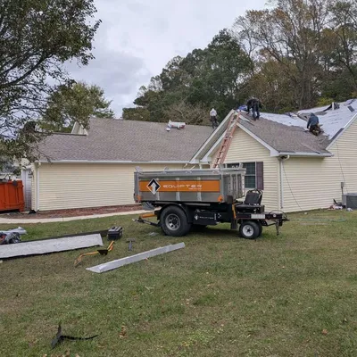 Roof tear-off in progress with a dump trailer staged in the yard by Eastern Shore Roofing and Remodeling