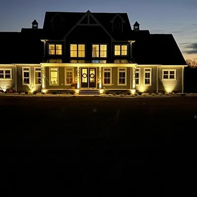 Landscape lighting illuminating a home's exterior and covered porch at dusk, installed by Elzey Services in Delmar, MD
