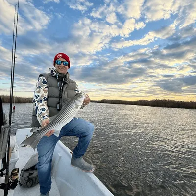 Captain holding a striped bass at sunrise on a FishPit Charters trip