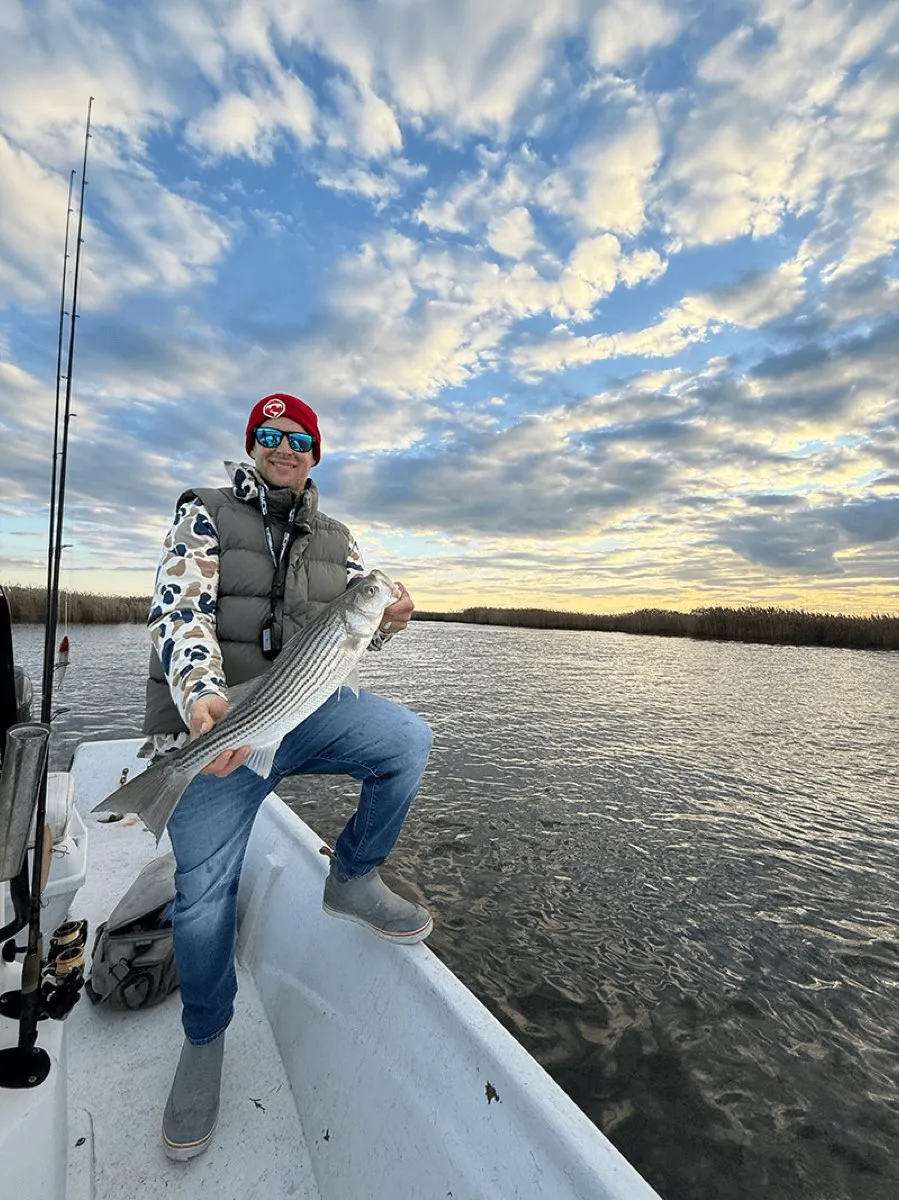 Captain holding a striped bass at sunrise on a FishPit Charters trip