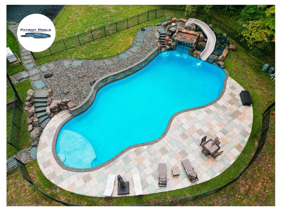 In-ground pool with a stone waterfall and slide feature built by Patriot Pools in a wooded backyard near Centreville, MD