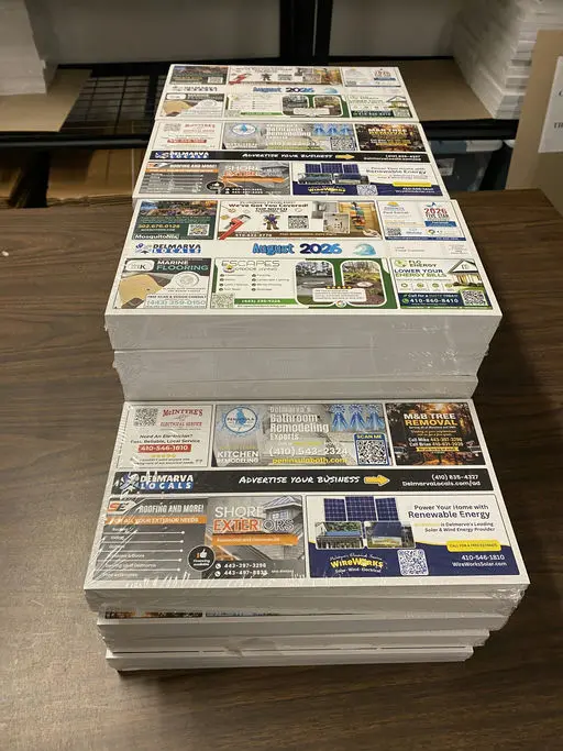 A stack of freshly printed Delmarva Locals community postcards showing local business ads