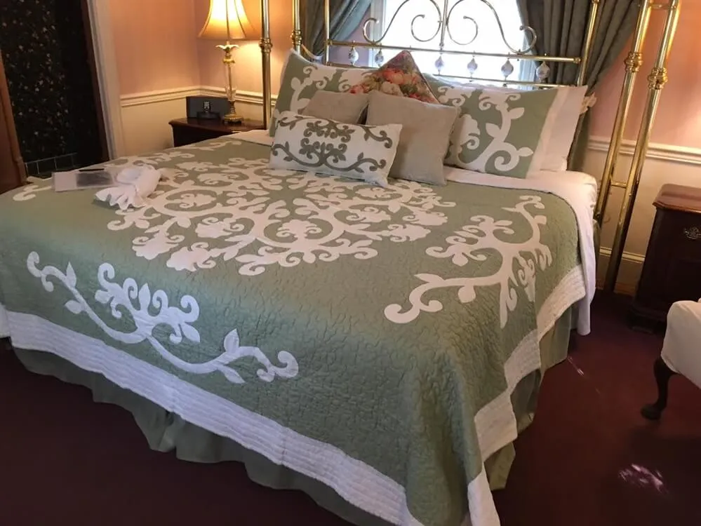Guest bedroom with a brass bed and sage green quilted bedspread at The Parsonage Inn in St. Michaels, MD