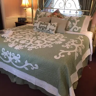 Guest bedroom with a brass bed and sage green quilted bedspread at The Parsonage Inn in St. Michaels, MD